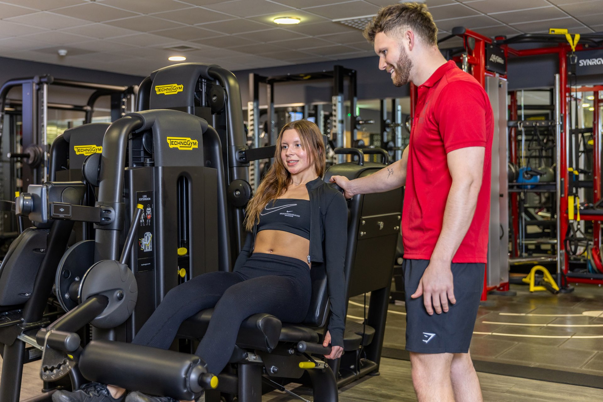 Male Fitness instructor coaching a famle member on the leg press in the gym at Westwoods health Club