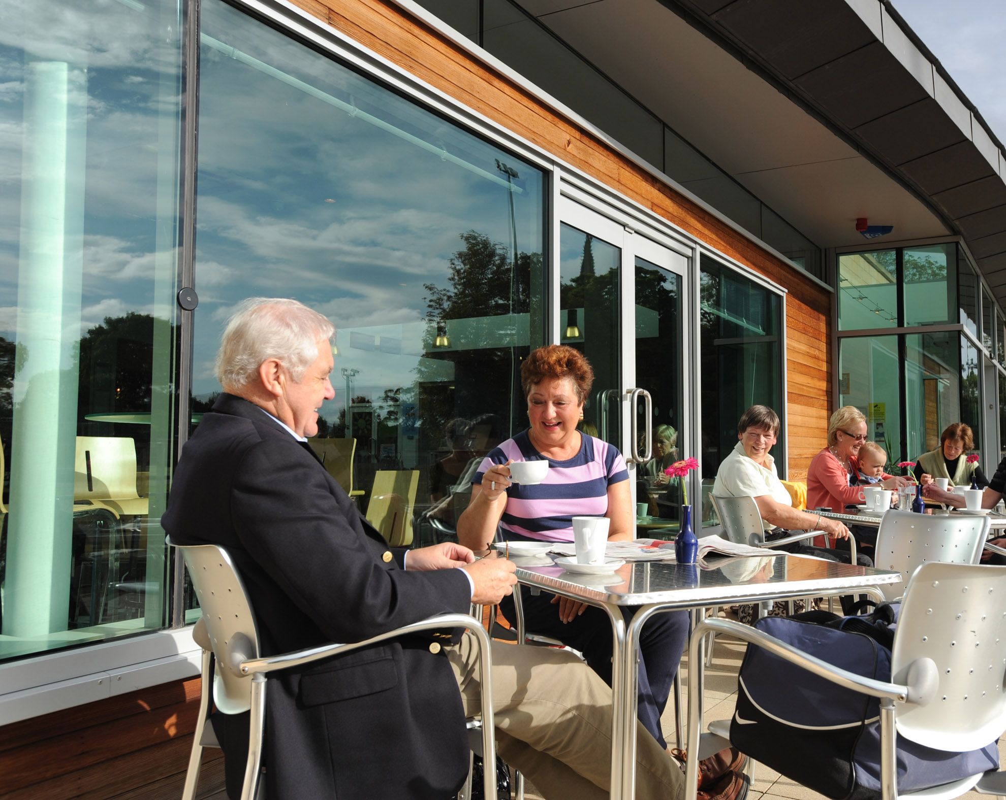 Members sitting outside on the terreace at westwoods health club, enjouying coffees whilst overlooking the tennis courts and fettescollege