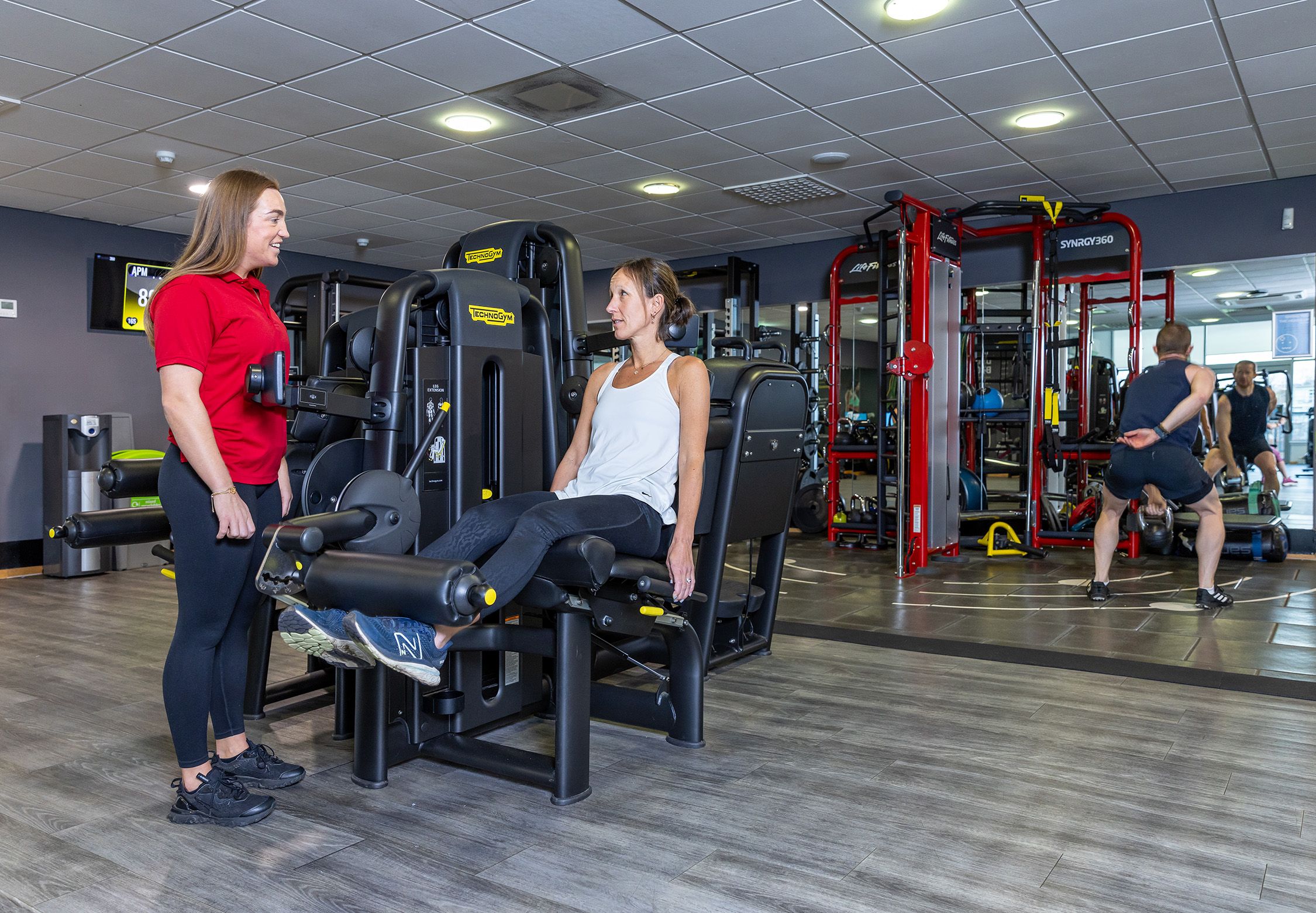 Female instructor speaking to a woman using leg extension machine