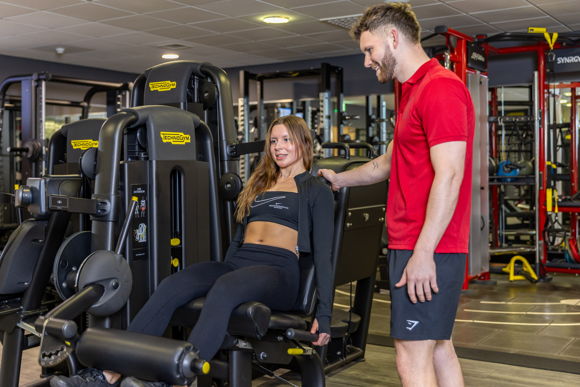 Male Fitness instructor coaching a famle member on the leg press in the gym at Westwoods health Club